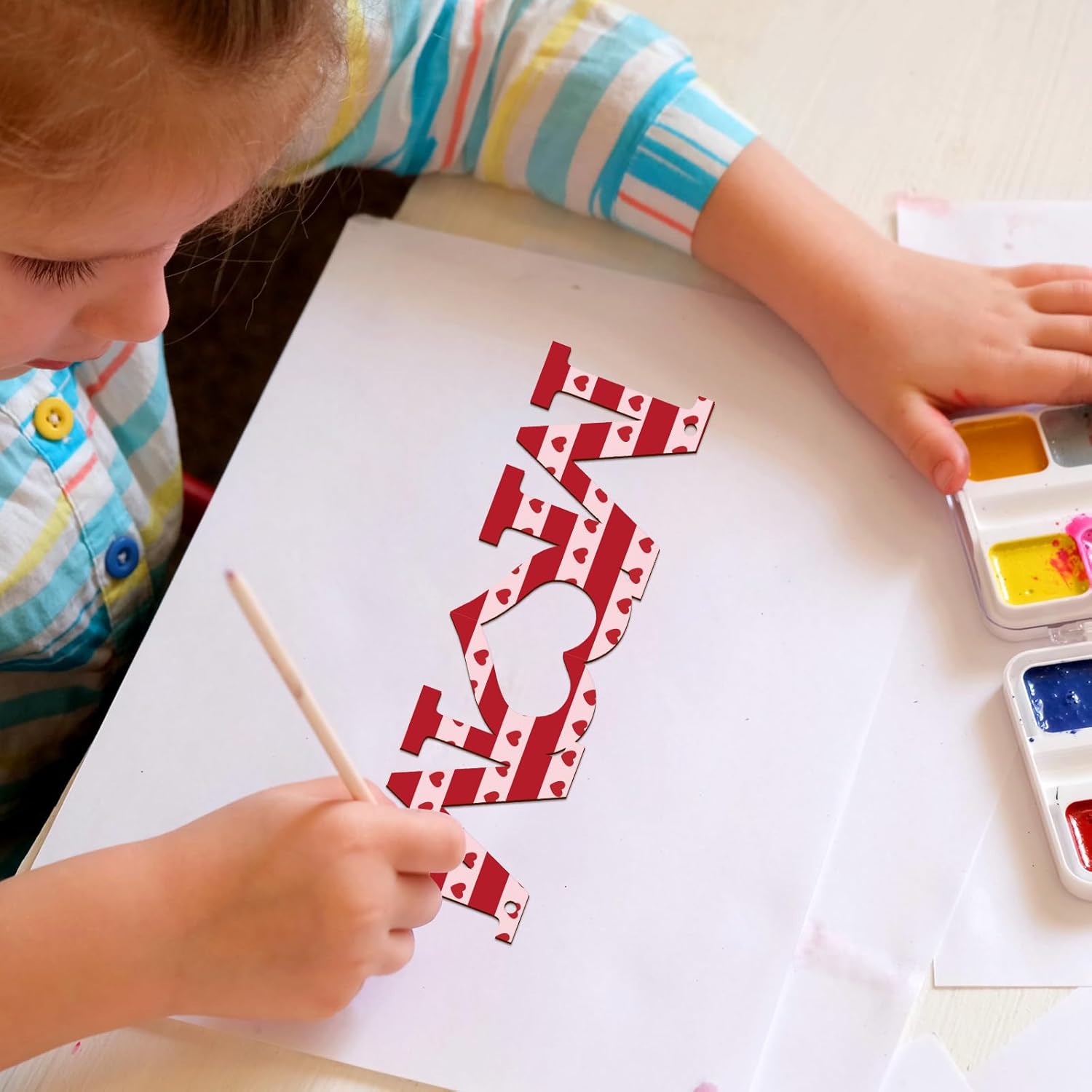 Child painting a red and white number on paper with watercolors.