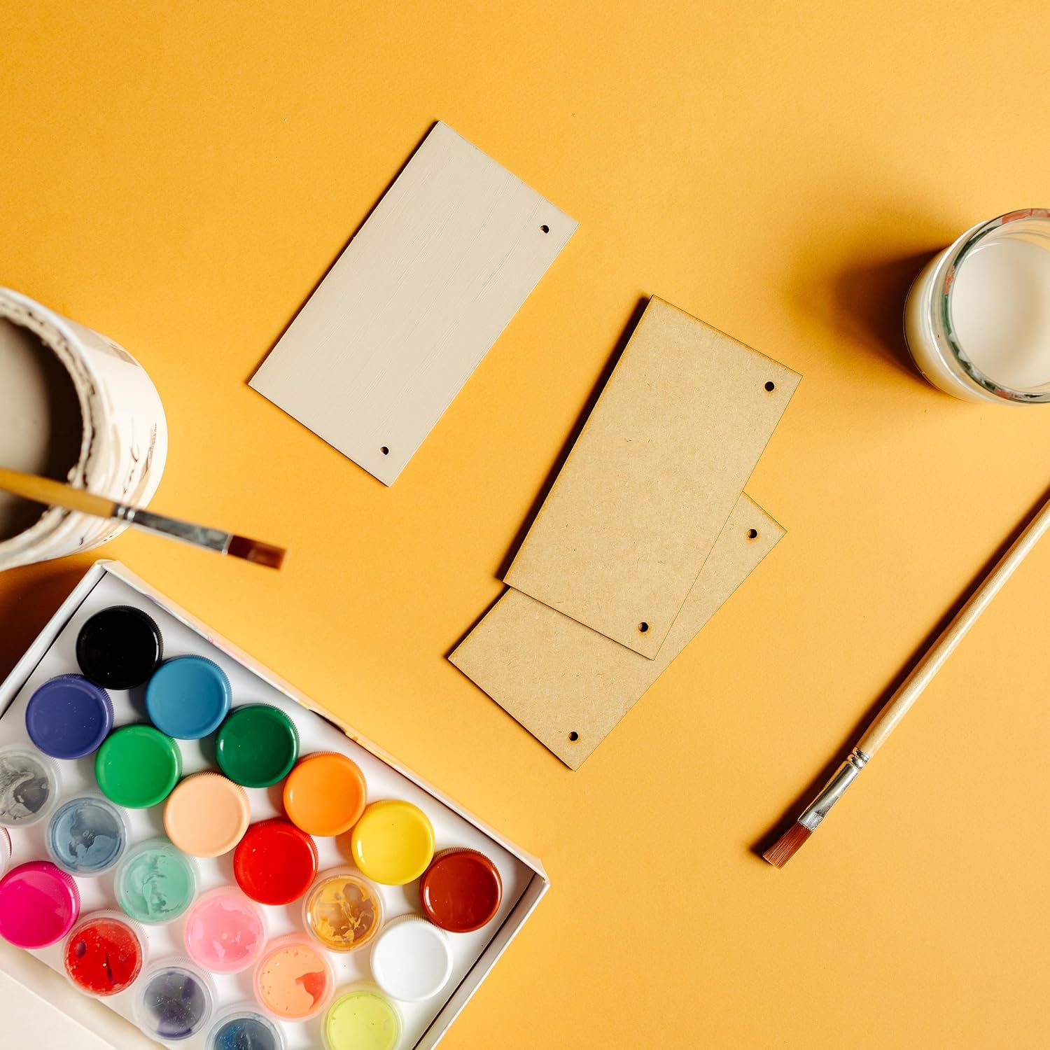 Art supplies including a paint palette, brushes, and a notepad on a yellow background