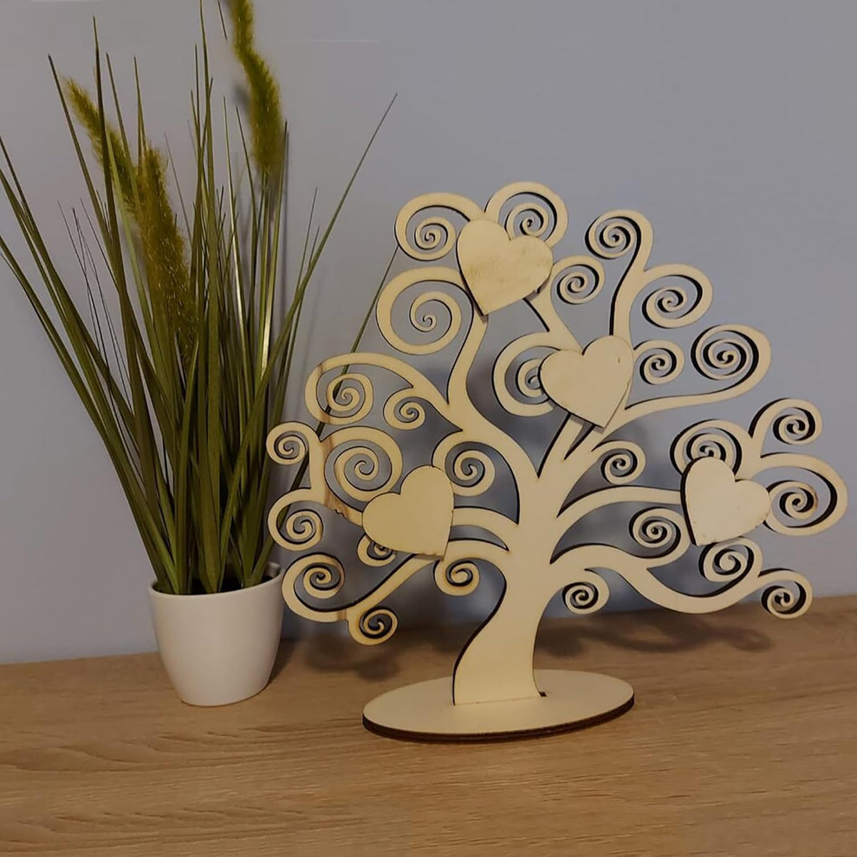 Wooden tree decorative item with heart shapes on a wooden surface next to a plant.