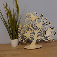Wooden tree decorative item with heart shapes on a wooden surface next to a plant.