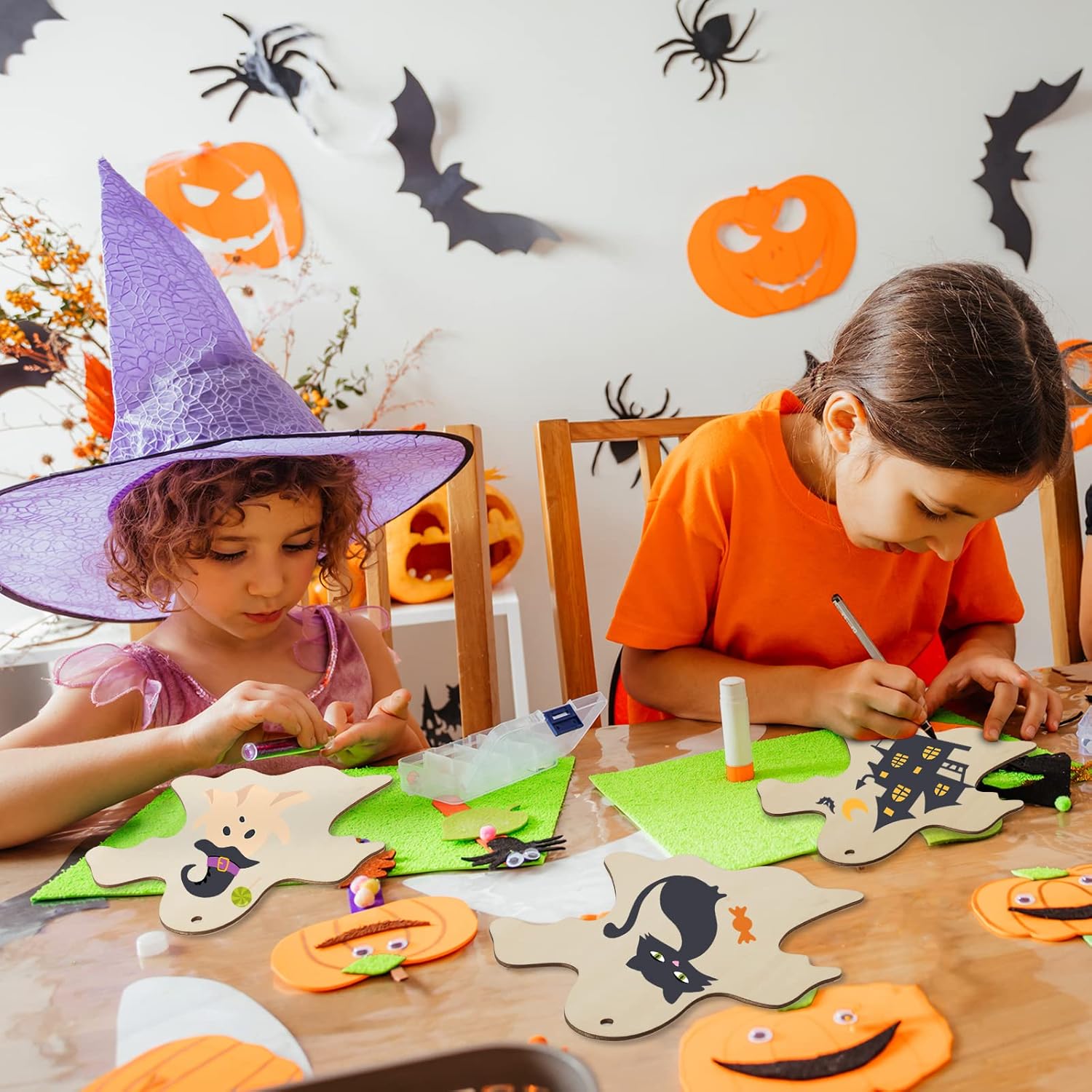 Two children in Halloween costumes sitting at a table with craft materials and decorations.