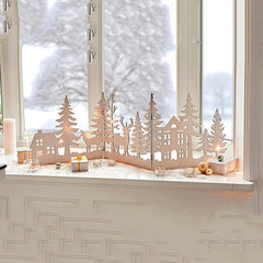 Decorative winter scene with cut-out trees, houses, and deer on a windowsill.