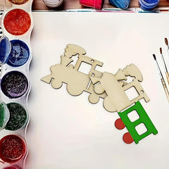 Wooden toy train model with a green engine and red wheels on a white surface, surrounded by paint containers and brushes.