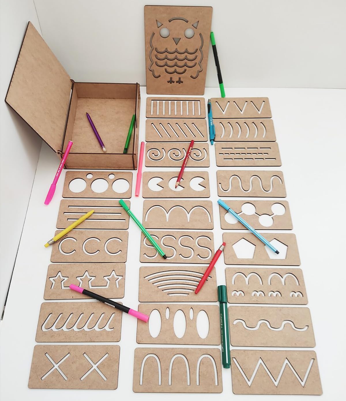 Cardboard stencils with various shapes and letters on a white surface with colored pencils.