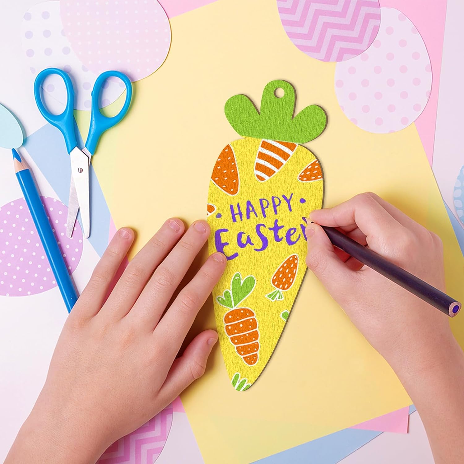 Child's hands decorating a yellow Easter card with colorful cutouts on a pink background.