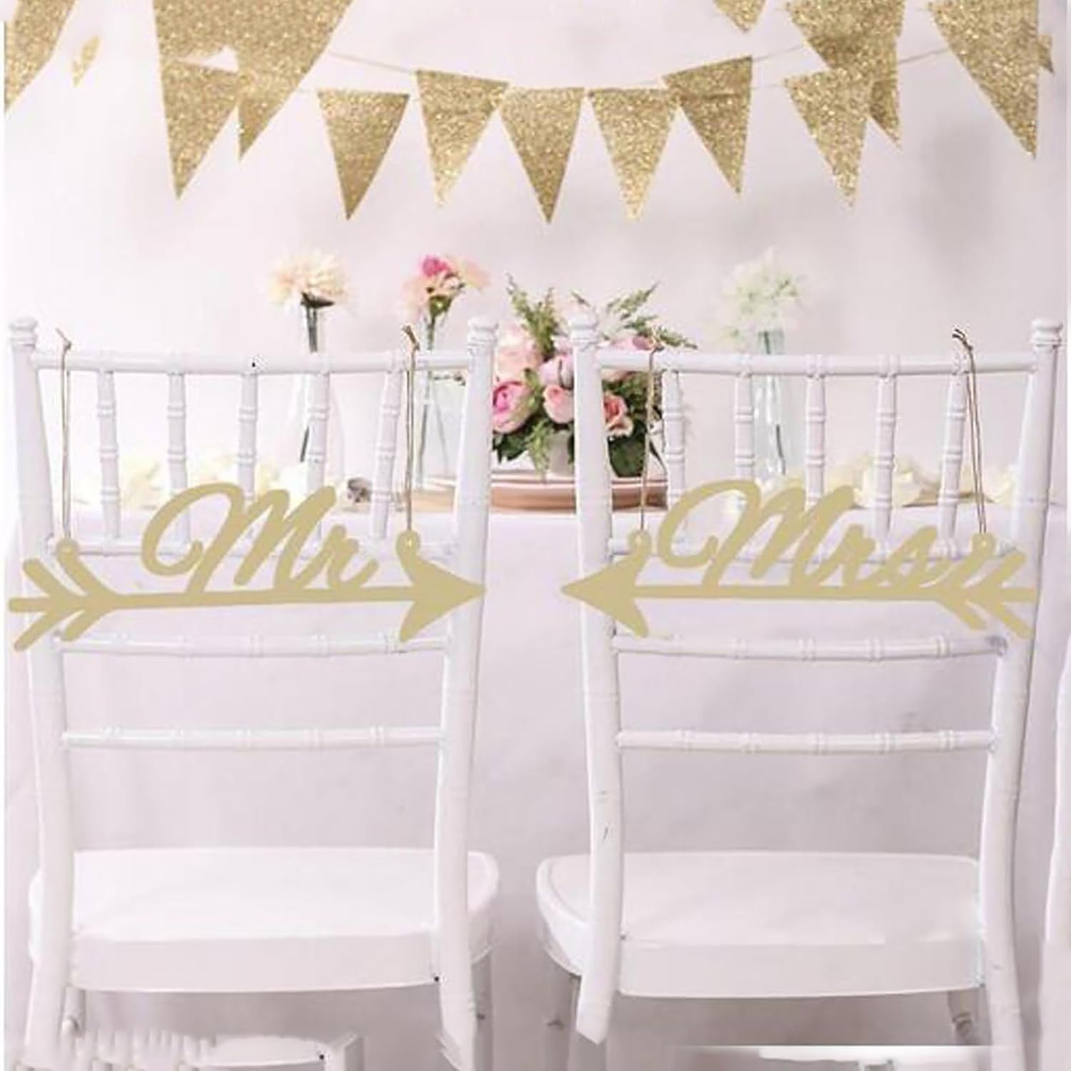 Decorated wedding setup with white chairs, gold 'Mr' and 'Mrs' signs, and floral arrangements.