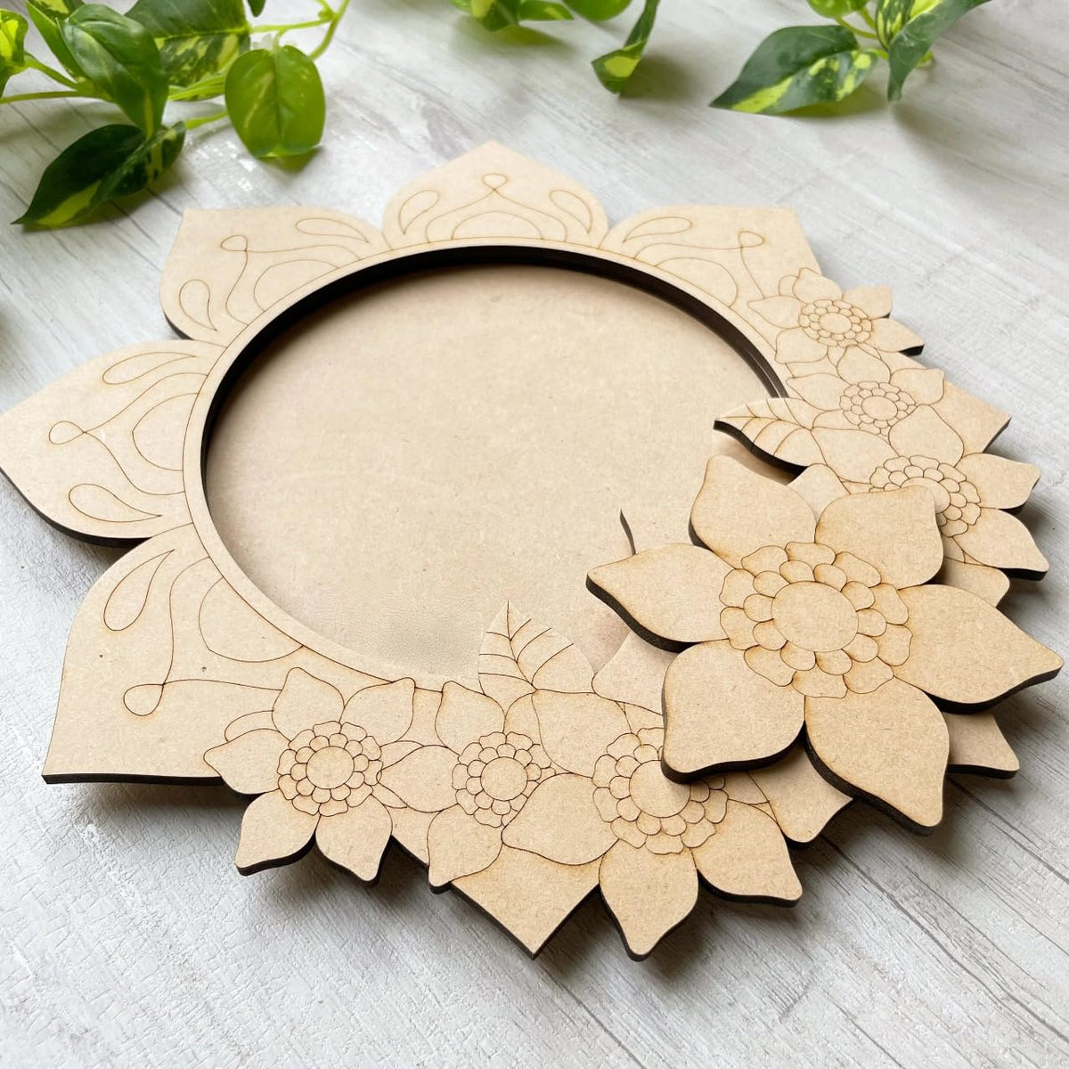 Wooden floral wreath cutout on a light wooden surface with green leaves in the background