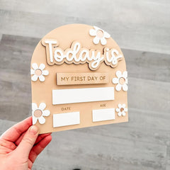 Wooden plaque with 'Today is my first day of' text and space for date and age on a gray background