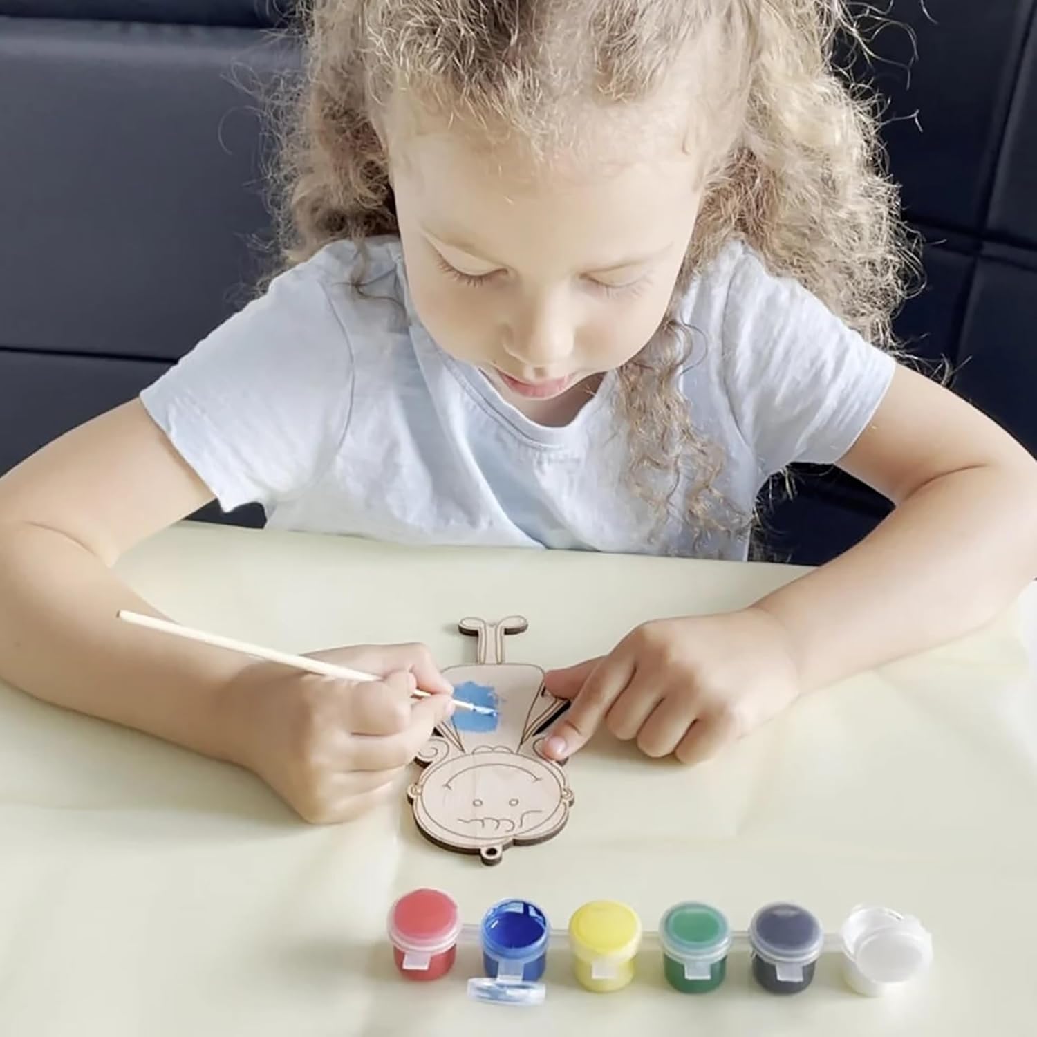 Child painting a decorative item with colorful paint containers on a table.