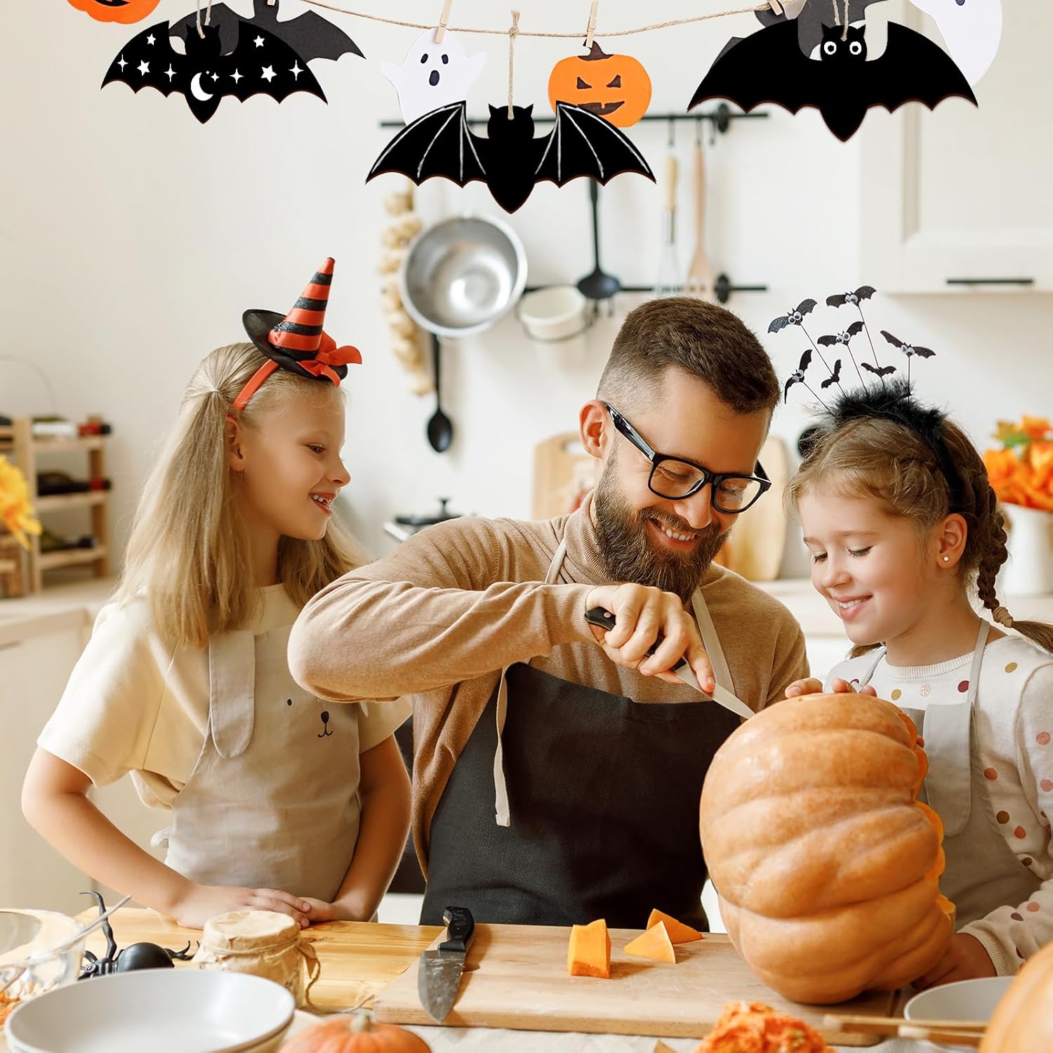 Man and two children in a kitchen preparing for Halloween, with pumpkins and decorations.
