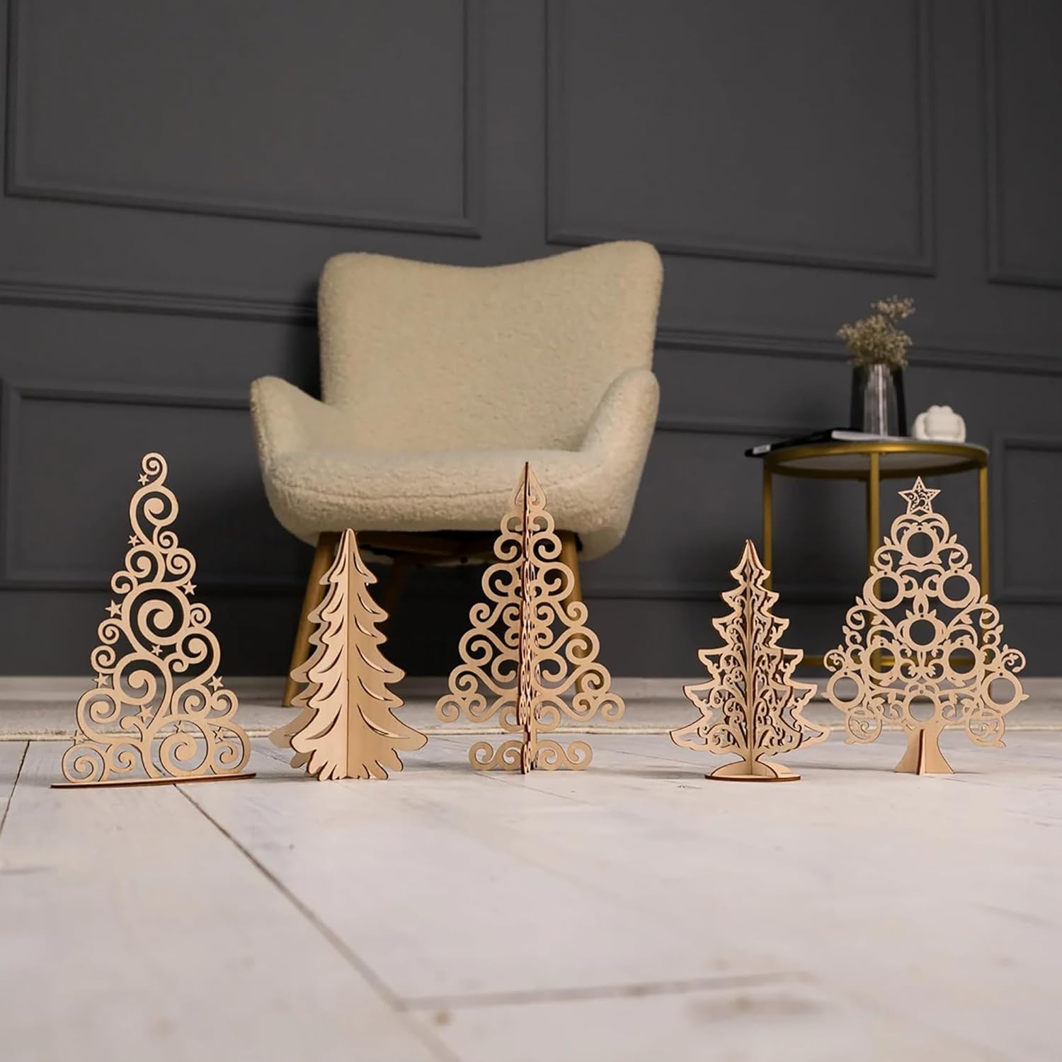 Set of decorative wooden Christmas trees on a marble surface with a chair and table in the background.