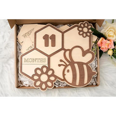 Wooden baby milestone card with bee design and '11 months' text, placed in a box.