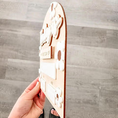 Wooden puzzle piece with cut-out design held by a hand against a wooden background