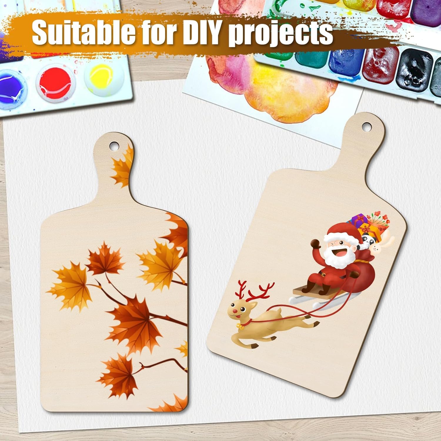 Two wooden cutting boards with autumn leaf and Santa Claus designs, surrounded by watercolor paints.