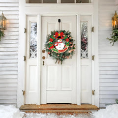 White door with a festive wreath featuring a snowman and red flowers, surrounded by snow.
