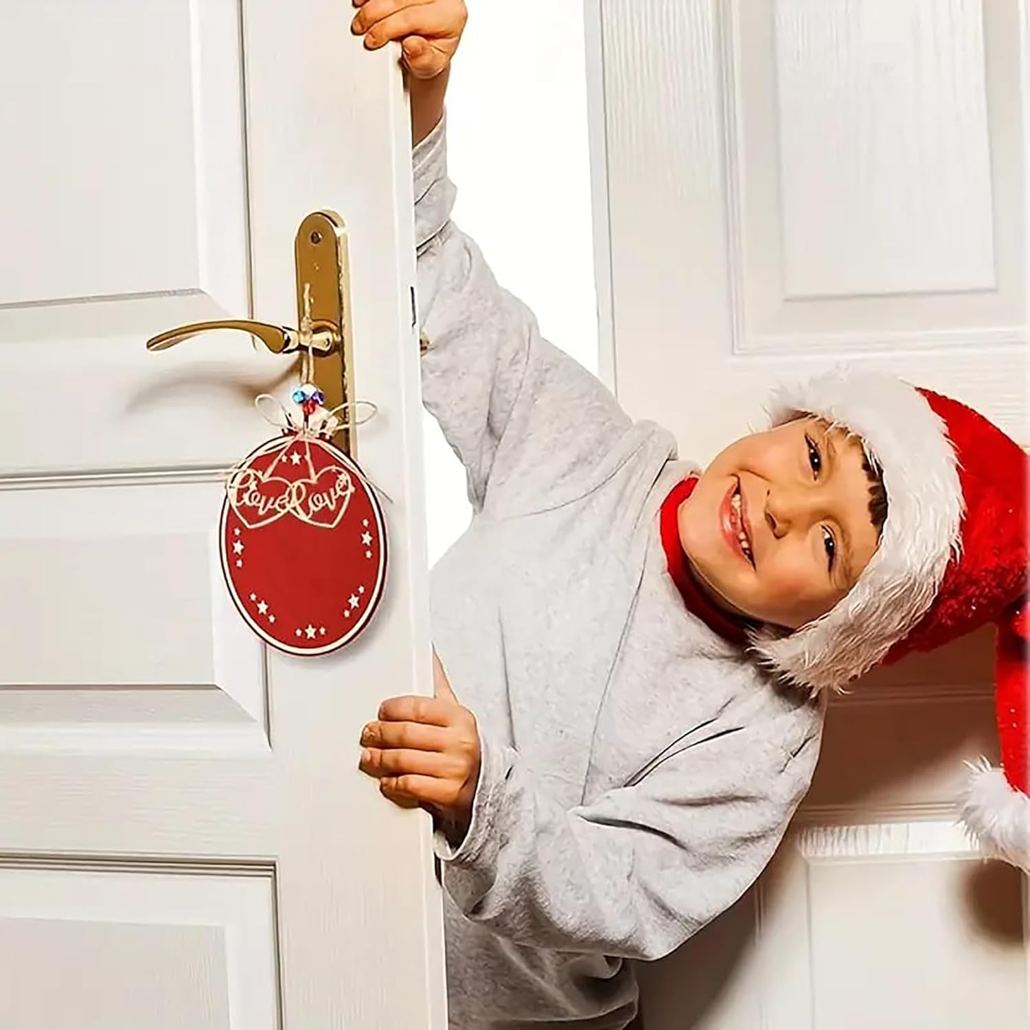 Child wearing a Santa hat peeking through a door with a Christmas decoration.