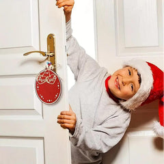 Child wearing a Santa hat peeking through a door with a Christmas decoration.