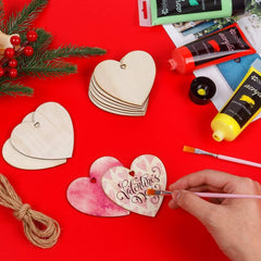 Hand painting a wooden heart ornament with 'Valentine's' on a red surface with art supplies.