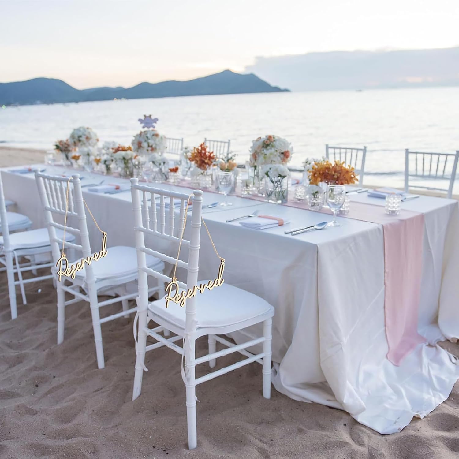 Decorated outdoor wedding table with chairs on a sandy beach.
