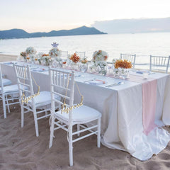 Decorated outdoor wedding table with chairs on a sandy beach.