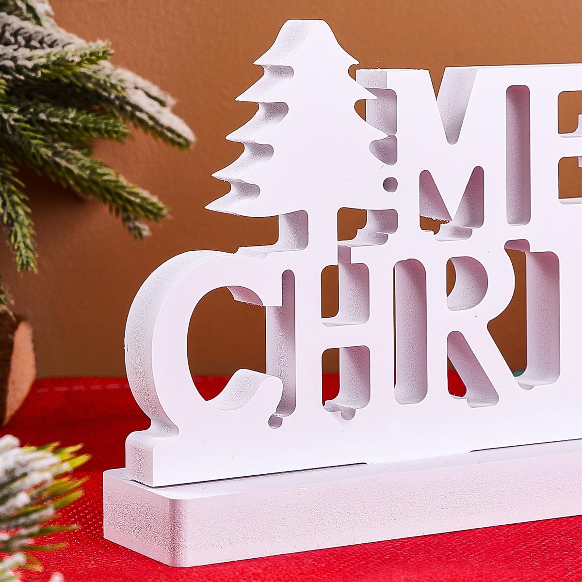 White decorative sign with 'Merry Christmas' text on a red surface with a brown background