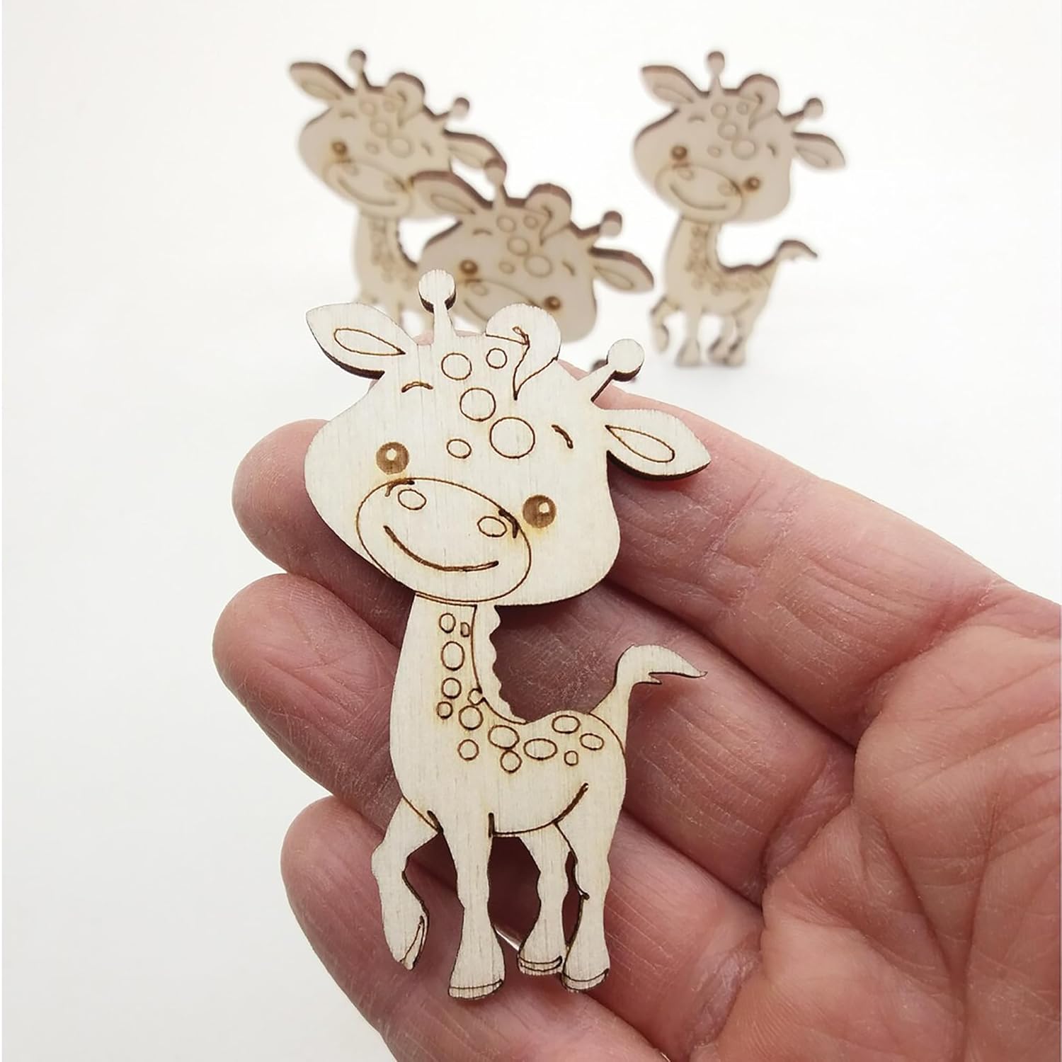Hand holding a small wooden giraffe ornament with two more in the background on a white surface.