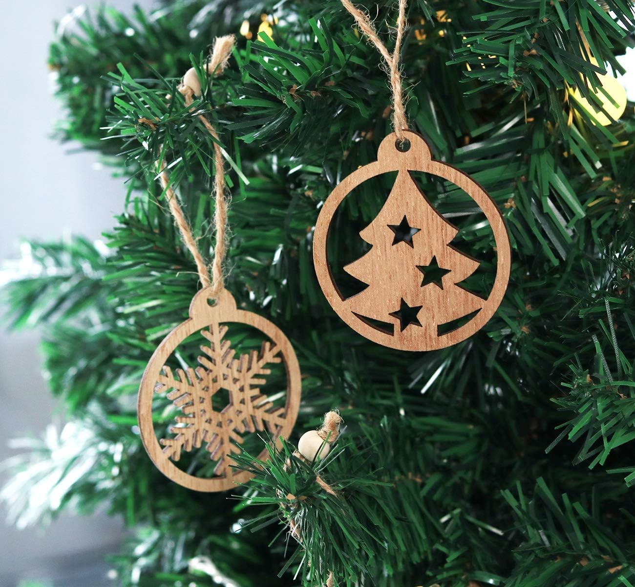 Wooden Christmas tree ornaments with snowflake and tree designs hanging on a green tree.