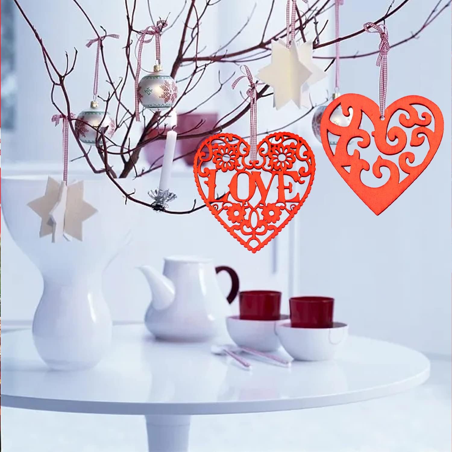 Decorative heart-shaped 'LOVE' ornament hanging from a branch with a white table and teacup set in the background.