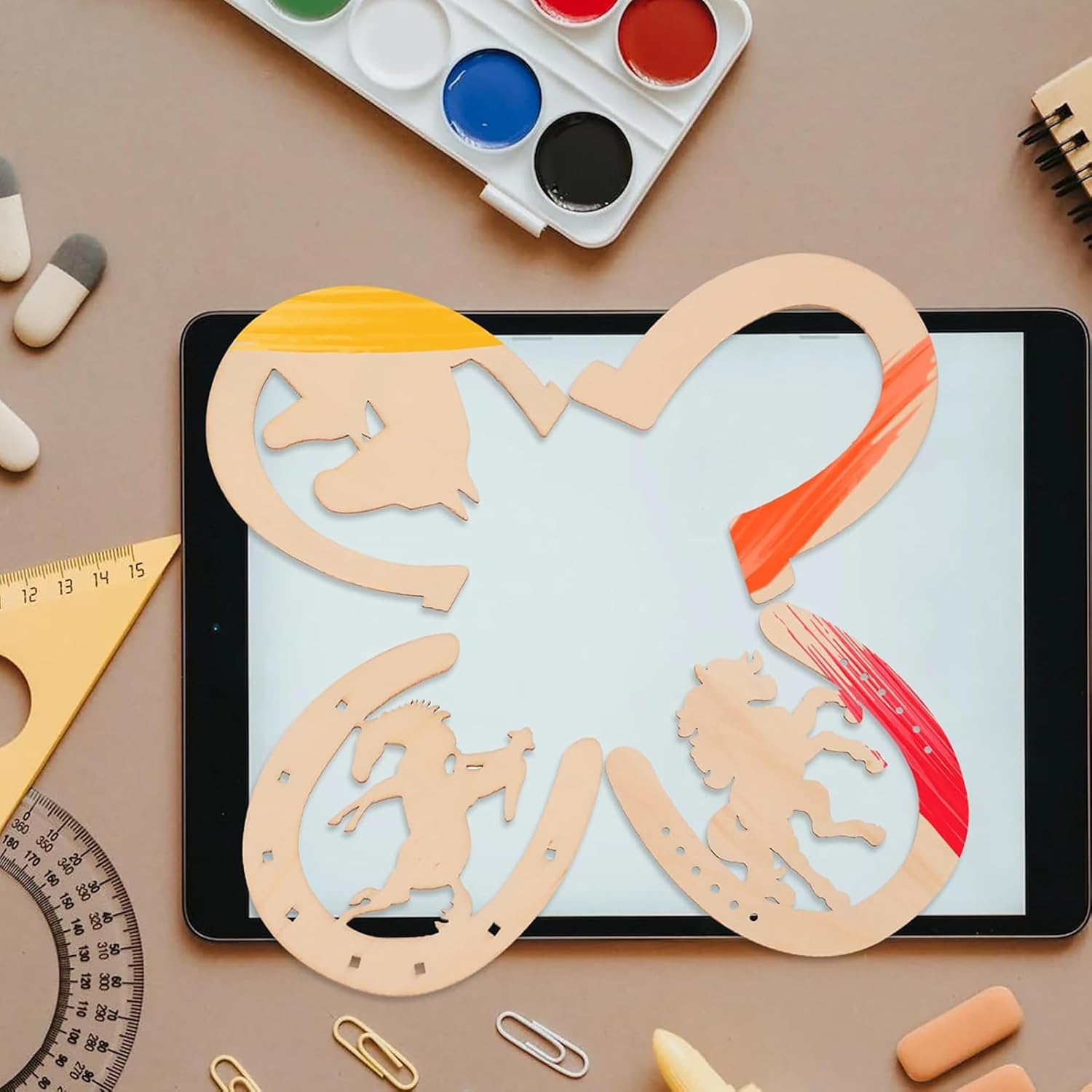 Wooden puzzle with animal shapes on a tablet screen, surrounded by art supplies on a brown surface.