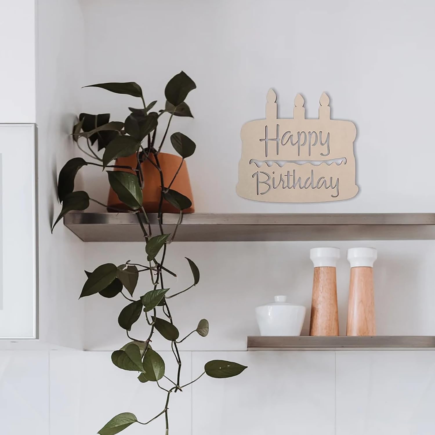 Wooden 'Happy Birthday' sign on a shelf with a plant and decorative items.