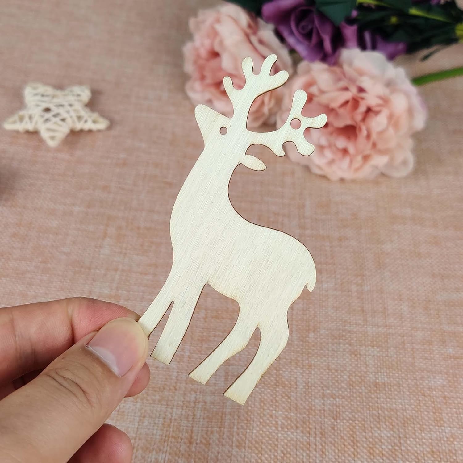 Wooden deer ornament held by a hand with flowers in the background