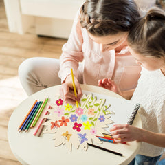 Two children coloring a picture of flowers on a table with colored pencils.