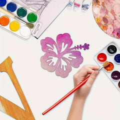 Artistic activity with watercolor paints, brushes, and a purple flower design on a white surface.