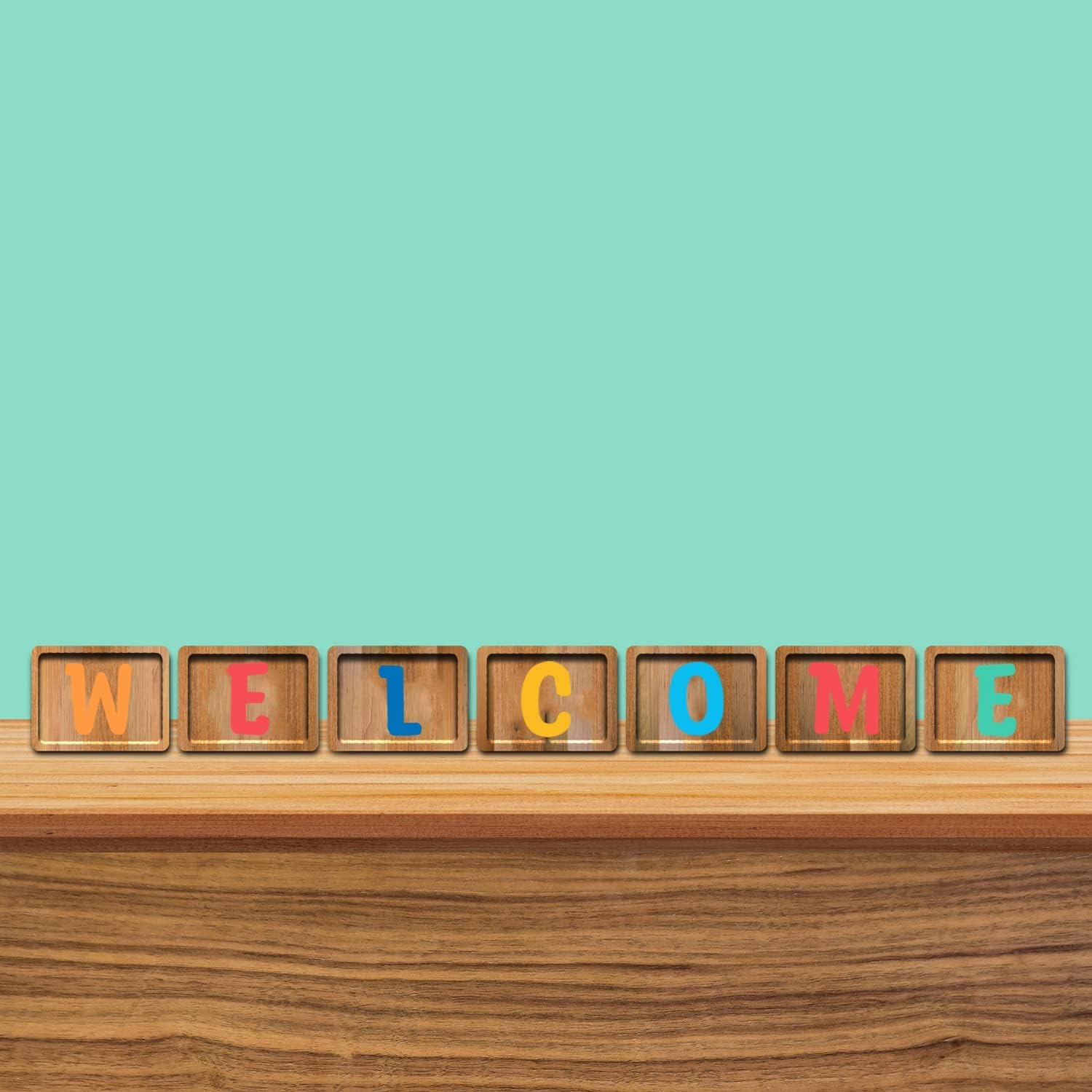 Wooden blocks with colorful letters spelling 'WELCOME' on a wooden surface with a teal background