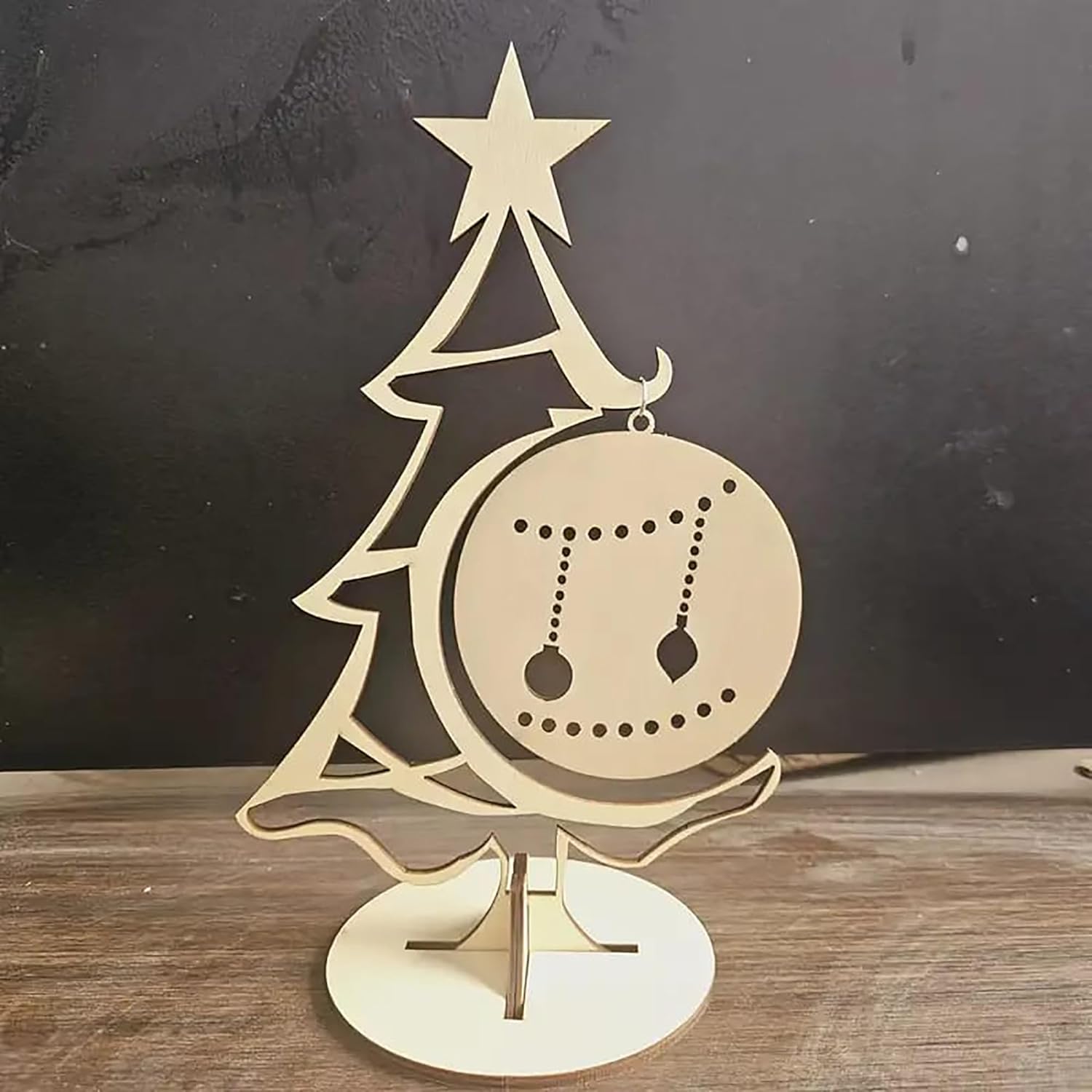 Decorative Christmas tree ornament with a star on top and a ball with cut-out designs, placed on a wooden surface.