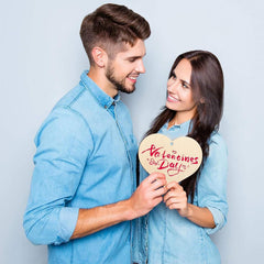 Man and woman holding a 'Valentine's Day' heart-shaped sign against a light blue background