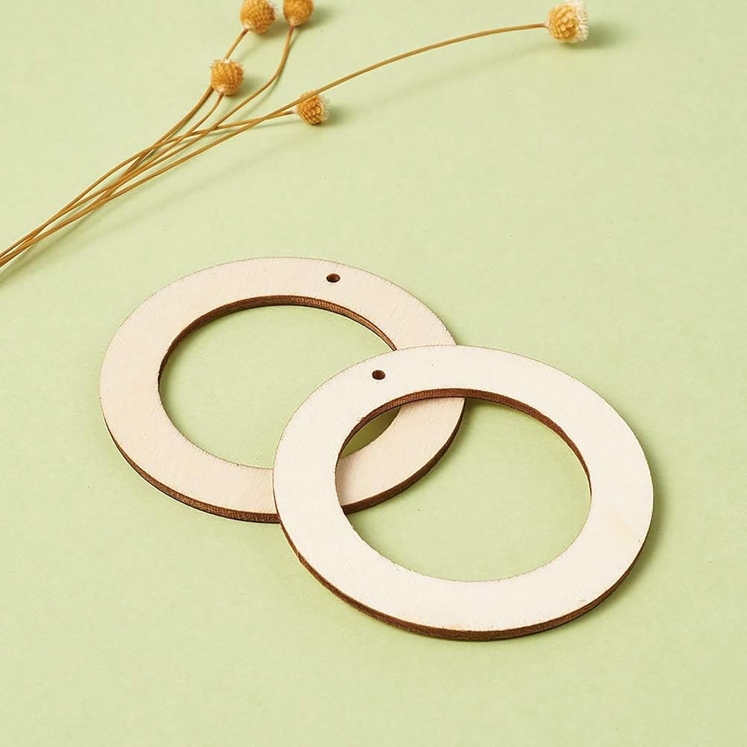 Two wooden rings on a light green background with dried flowers.