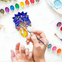 Person painting a colorful pine cone with watercolors on a white surface.