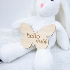 White plush bunny with a wooden butterfly-shaped 'hello world' tag on a soft white background