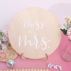 Round wooden sign with 'Miss to Mrs.' text on a pink background with decorative elements.