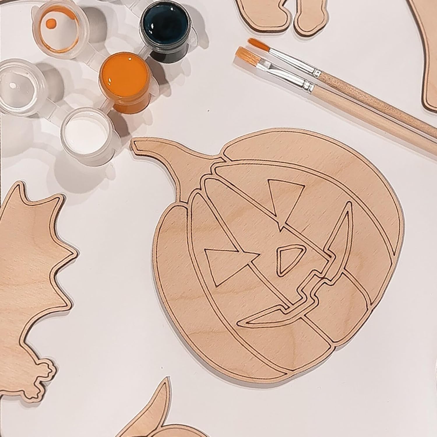 Wooden pumpkin and bat cutouts with paint cans and brushes on a white background
