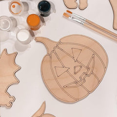 Wooden pumpkin and bat cutouts with paint cans and brushes on a white background
