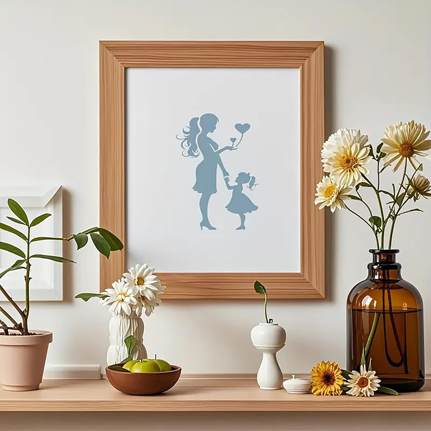 Framed artwork of a silhouette of a woman and child holding hands with flowers, displayed on a shelf with decorative items.
