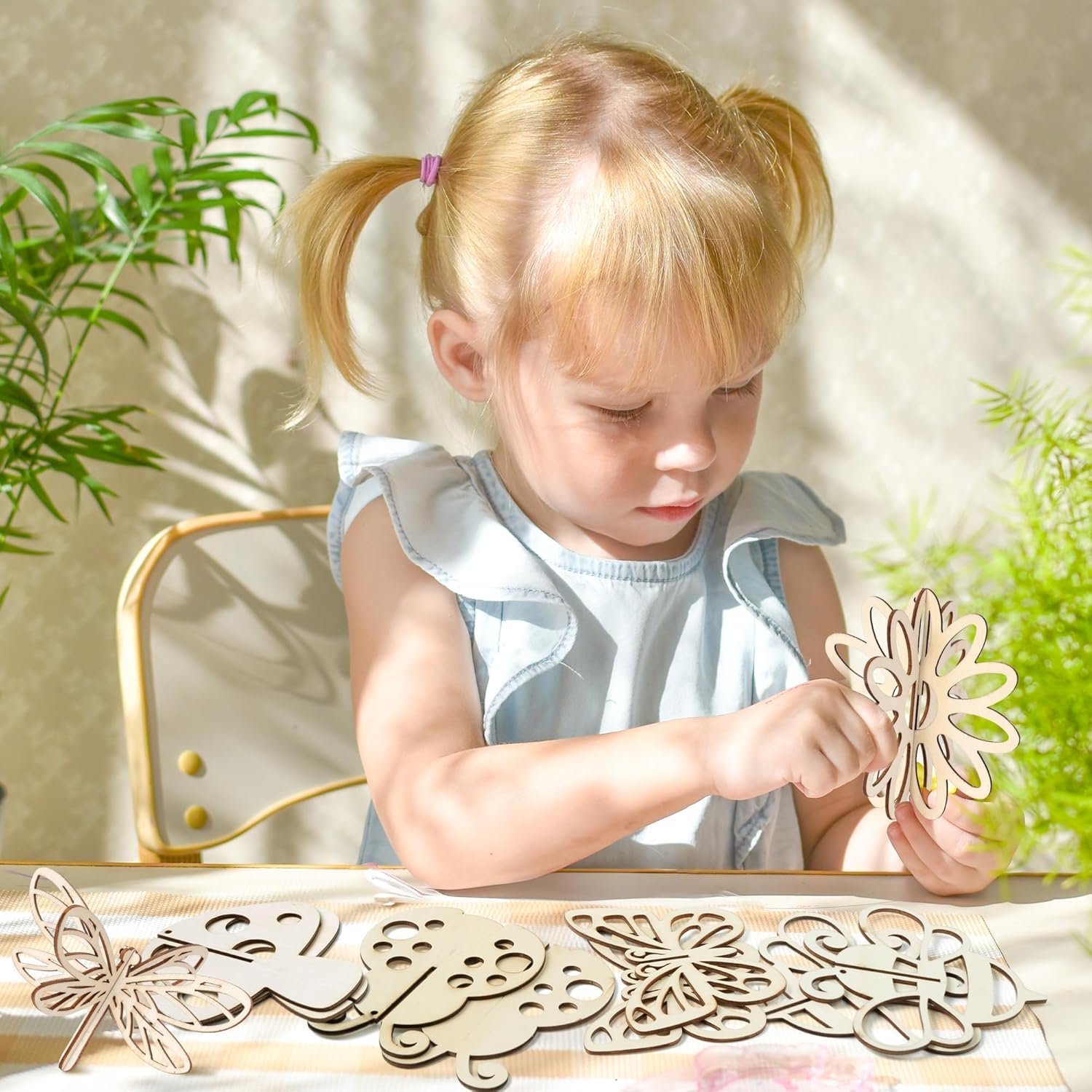 Child playing with wooden cutouts on a table with plants in the background