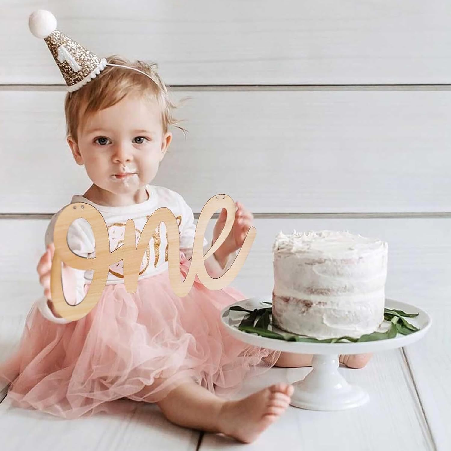 Child celebrating a first birthday with a cake and 'one' sign.