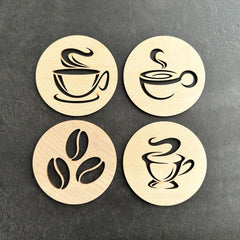 Four wooden coasters with coffee-themed designs on a dark surface