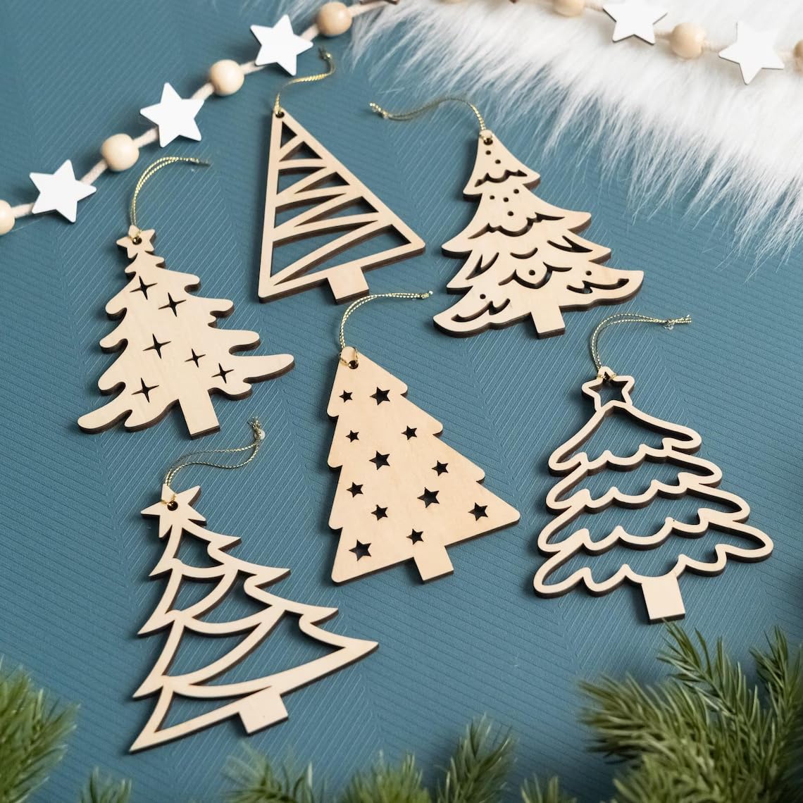 Wooden Christmas tree ornaments on a blue surface with greenery and stars.