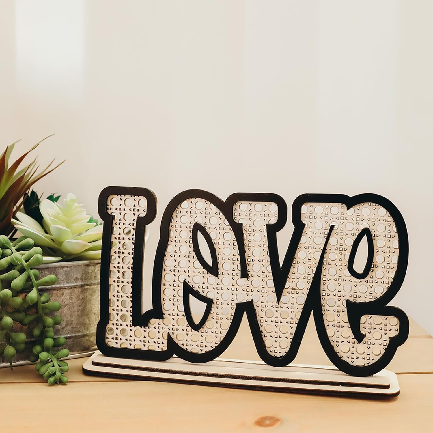 Decorative sign with 'LOVE' on a wooden surface with plants in the background