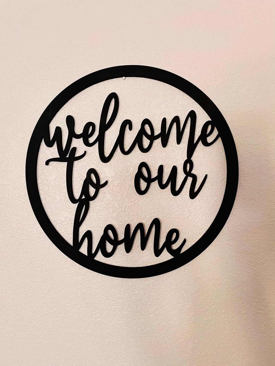 Decorative metal sign with 'welcome to our home' text on a beige background