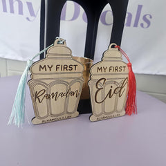 Two wooden ornaments with tassels, one saying 'My First Ramadan' and the other 'My First Eid', on a white surface.